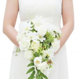 Bride in a white dress holding a cascading white rose bouquet with green accents