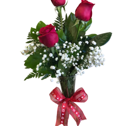 Three red roses in a clear vase with baby's breath and a red ribbon