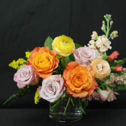 Bouquet of orange, yellow, and pink roses in a clear glass vase