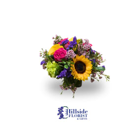 Colorful mixed bouquet with sunflower, pink rose, and purple accents in a glass vase