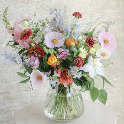 Loose garden-style bouquet of mixed pastel and bright flowers in a clear glass vase.