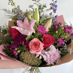 Hand-tied bouquet of pink lilies, roses, and mixed blooms wrapped in pink and kraft paper