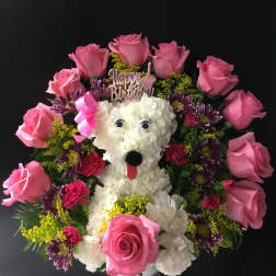Pink rose and white flower arrangement shaped like a dog with a birthday topper
