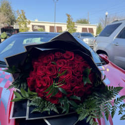 Bouquet of red roses wrapped in black paper on a car hood