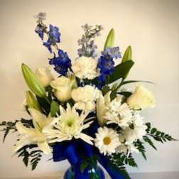 White and blue floral arrangement in a glass vase with a blue ribbon