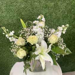 Bouquet of pale yellow roses and white lilies in a square glass vase