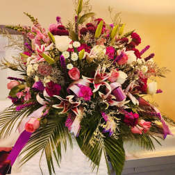 Large pink and white floral spray with ribbons on a casket