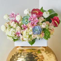 Mixed floral arrangement in a white container on a gold vase