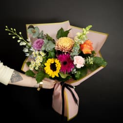 Mixed bouquet with sunflower, roses, and chrysanthemums wrapped in pink paper