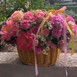 Pink and peach flowers arranged in a wicker basket with ribbon.