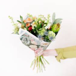 Handheld bouquet with peach, green, and blue flowers in floral wrap