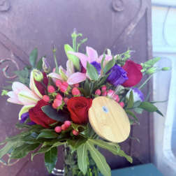 Bouquet of red roses, pink lilies, and purple blooms in a glass vase