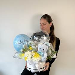 Baby gift arrangement with balloons, flowers, and a teddy bear in a white box
