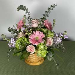 Pink gerbera daisies and roses in a woven basket with lavender accents