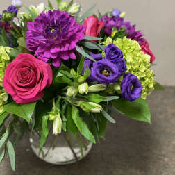 Bouquet of pink roses, purple blooms, and green hydrangeas in a glass vase