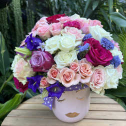 Mixed roses and purple flowers in a face-shaped vase with a polka-dot ribbon