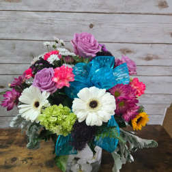 Mixed bouquet with roses, daisies, and a blue ribbon in a glass vase