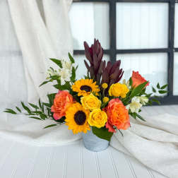 Mixed bouquet of yellow roses, sunflowers, and coral blooms in a metal container