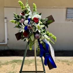 Standing floral wreath with white lilies, red roses, and blue ribbon on an easel