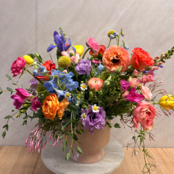 Colorful mixed flower arrangement in a blush ceramic vase on a marble stand