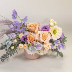Pastel bouquet of roses, poppies, and purple blooms in a pink vase