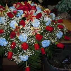 Large floral spray with red roses, blue carnations, and lilies