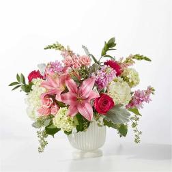 Pink lilies and roses arranged in a white vase with pale hydrangeas
