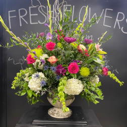 Large mixed floral arrangement in a white urn vase with pink, white, and purple blooms