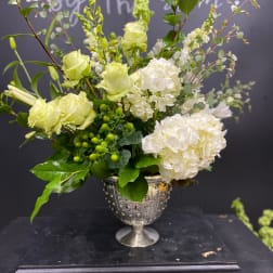 Green and white floral arrangement in a silver urn vase