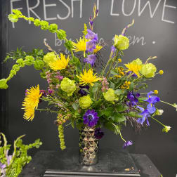 Tall mixed bouquet in a metallic vase with yellow, purple, and green flowers