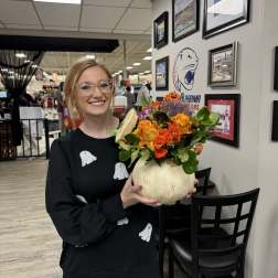Woman holding a pumpkin vase filled with orange and purple flowers