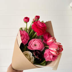 Handheld bouquet of pink and red ranunculus wrapped in kraft paper