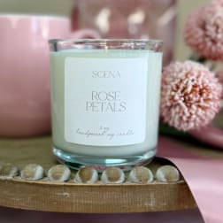 Rose-scented white candle in a clear glass jar with pink mug, flowers, and ribbon on a wooden tray