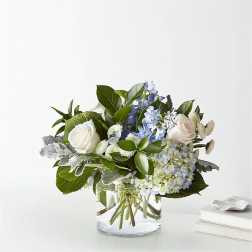 White roses and blue flowers in a clear glass vase