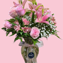 Pink roses and lilies arranged in a glass vase with a ribbon