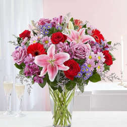 Mixed bouquet of roses, lilies, and daisies in a clear glass vase