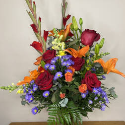 Mixed bouquet of red roses, orange lilies, and purple daisies in a clear vase