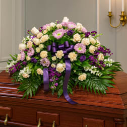 Purple and cream floral casket spray with ribbon on a wooden casket