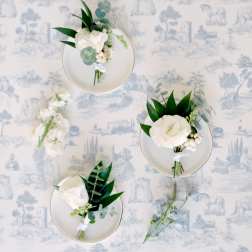Small white floral boutonnieres on plates with dark green leaves