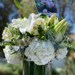 White floral arrangement in a glass vase with lilies and hydrangeas