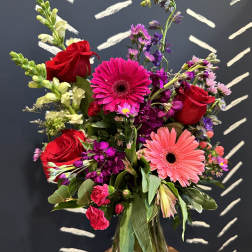 Mixed bouquet of red roses, pink gerbera daisies, and purple flowers in a glass vase