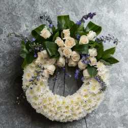 White floral wreath with cream roses and purple accents on a stand