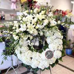 Large white floral wreath on a stand with lilies and roses