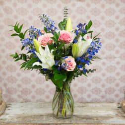 Pink roses and white lilies in a clear glass vase with blue flowers