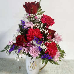 Mixed red, pink, and purple flowers arranged in a white mug vase