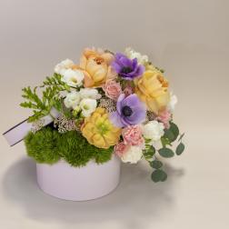 Pastel flower arrangement in a round pink box with purple and peach blooms