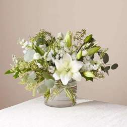 White lilies and delicate white blooms arranged in a clear glass cylinder vase