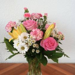 Pink roses, yellow lilies, and white daisies in a glass vase