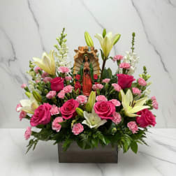Pink roses and lilies arranged around a religious figurine in a rectangular vase
