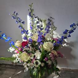 Mixed bouquet of white roses, blue delphinium, and pink flowers in a glass vase